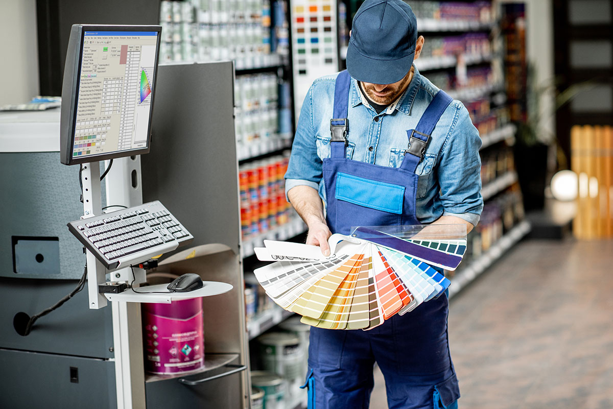 Portrait of a workman with color swatches near the equipment for coloring in the building shop