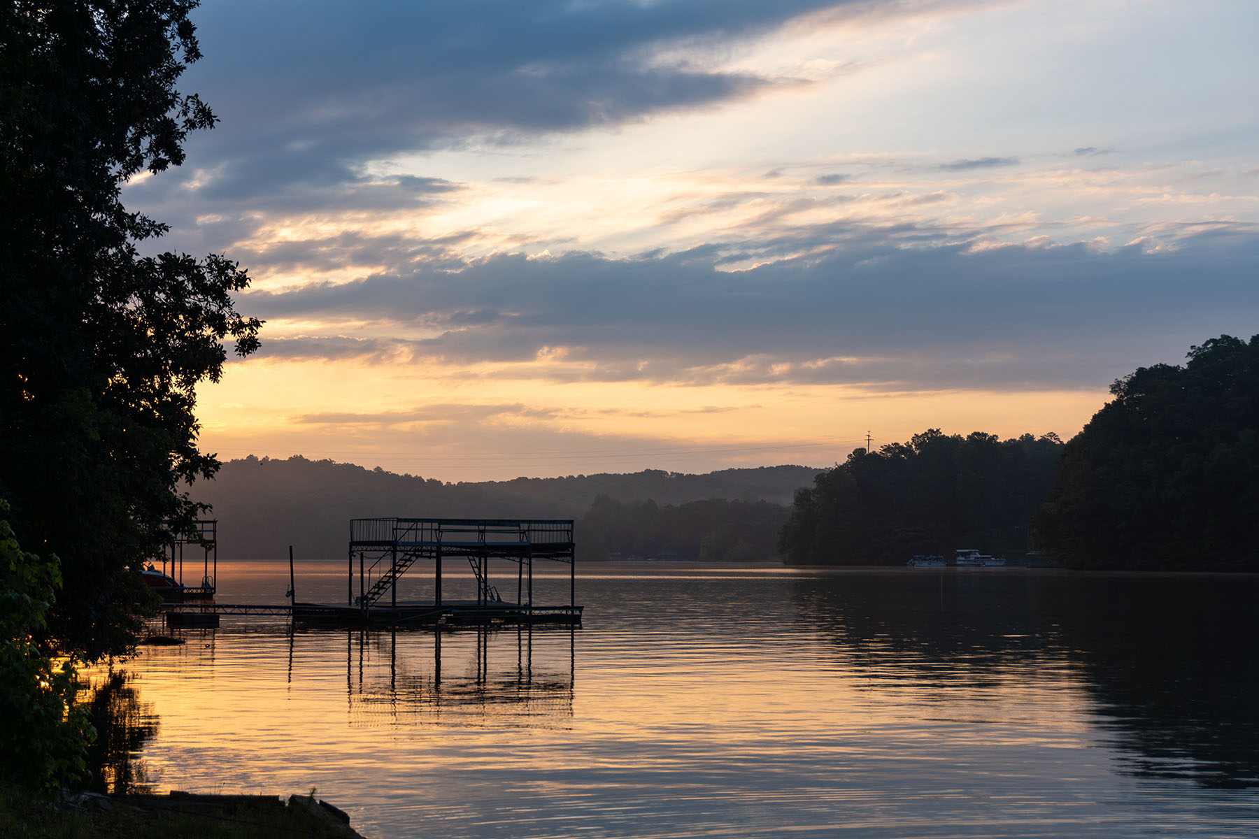 Dawn over Lake Lanier; silhouette of a dock and trees on a lake under a purple and orange sky with clouds; landscape view