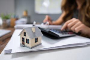 Close-up Of A Person Hand Calculating A Real Estate Property Tax On Wooden Desk