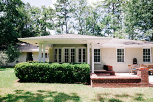 Rear view of house home with brick and concrete patio and landscaped bushes